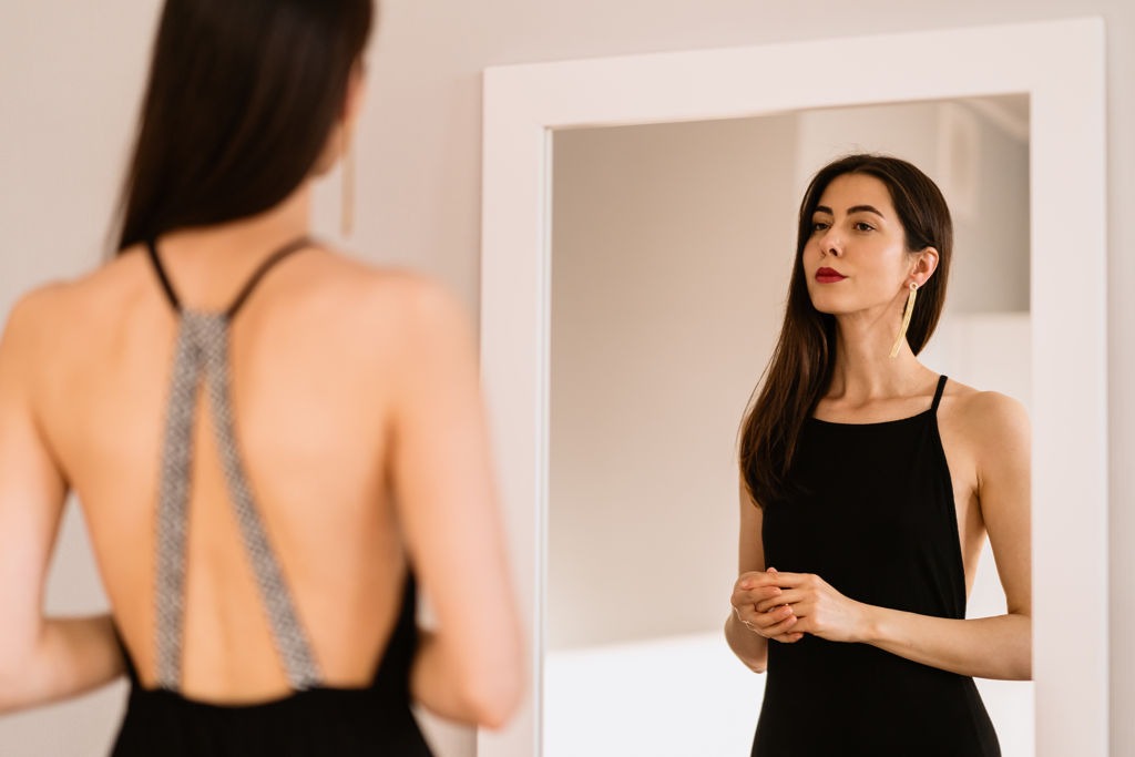 młoda kobieta w czarnej sukience przed lustrem